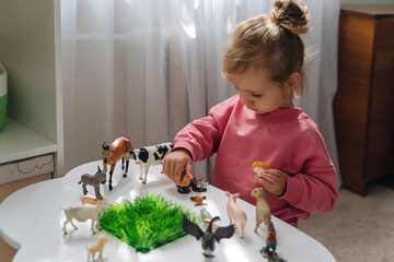 A little girl playing with farm animals on the table in nursery. Educational game. Learning through...