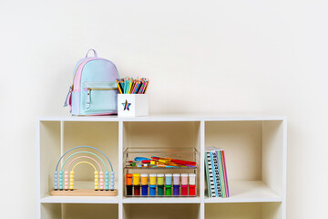 White shelving with kids backpack and various material for creativity and art activity. Stationery and supplies for drawing and craft. Organizing and storage in childrens room.
