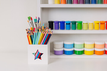 Obraz premium Paints and pencils on white shelves. Stationery and supplies for drawing and craft. Various material for creativity and kids art activity. Organizing and storage in craft room.