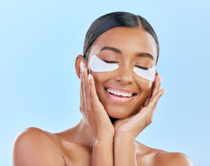 Beauty, eye patch and face of a woman with natural skin glow on a blue background. Dermatology, collagen mask and cosmetics of Indian female model for facial shine and touch for self care in studio