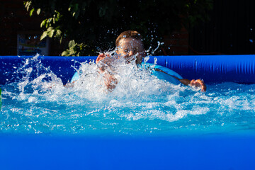 A child splashes in the pool on a summer sunny day. Mila happy boy bathes in the pool on a hot day....