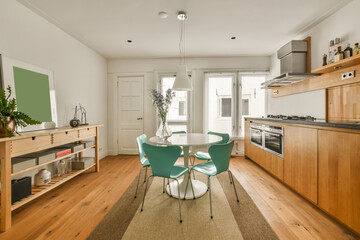 a kitchen and dining area in a small apartment with wood flooring, white walls, wooden cabinets and green chairs