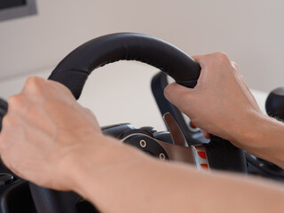 A person sitting behind a computer and holding the steering wheel of a driving simulator
