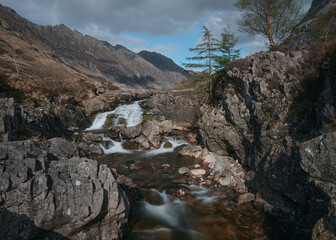 Waterfall on the rocky River Coe and and a spruce tree. Glencoe Mountain, Scotland, United Kingdom
