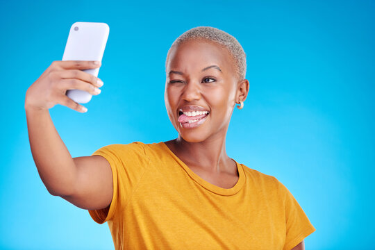 Social media, selfie and funny face with a black woman on blue background in studio to update her profile picture. Post, app and a happy young female influencer taking a photograph for her status