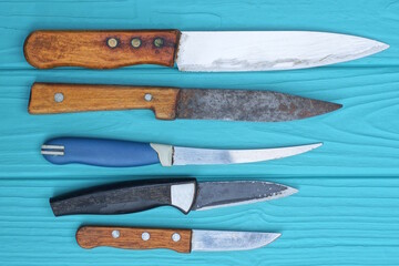a set of a row of different old colored table knives lie on a blue wooden table