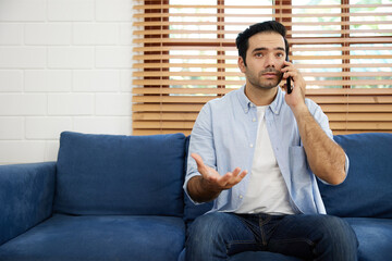 young handsome man sitting on sofa and talking by smartphone at home