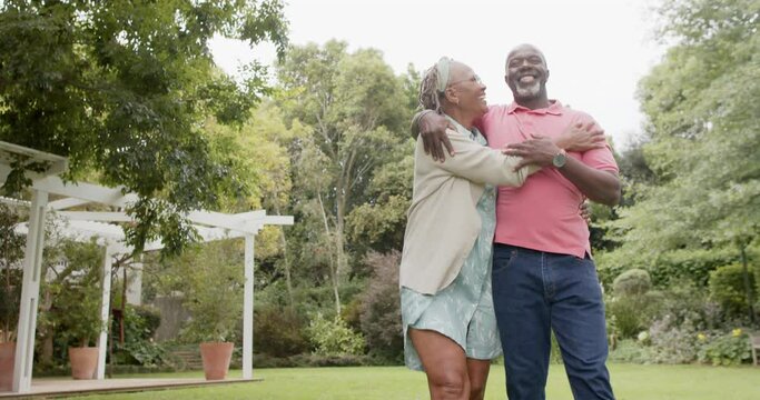 Happy senior african american couple embracing and walking in garden, slow motion