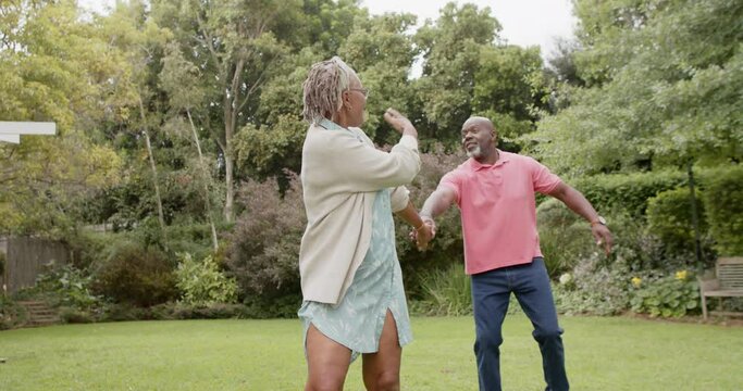 Happy senior african american couple holding hands and walking in garden, slow motion