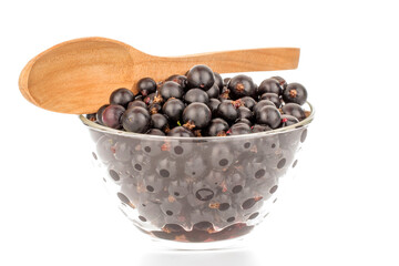 A few sweet black currant berries in a glass bowl with a wooden spoon, macro, isolated on a white background.