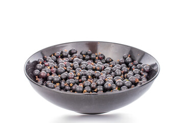 Several sweet black currant berries in a black ceramic plate, macro, isolated on white background.