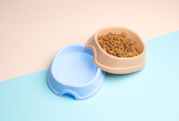 Pet bowl of dry food and water on pastel background. Top view