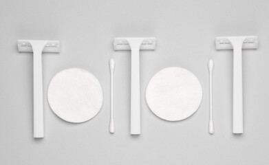 White razors with cotton pads and sticks on a gray background. Self-hygiene, beauty concept. Top view. Flat lay