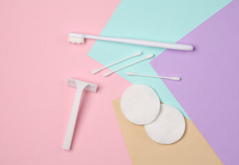 White razor with cotton pads and sticks, toothbrush on pastel background. Self-hygiene, beauty concept. Top view. Flat lay
