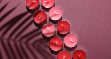 Aroma tea candles with palm leaf shadow on burgundy background. Top view. Copy space
