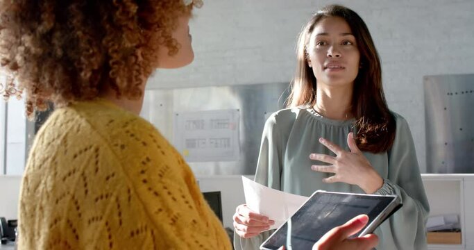 Happy diverse female colleagues with tablet and documents discussing work in office, slow motion