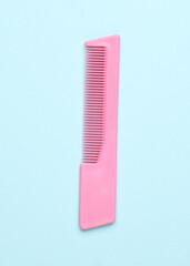 Pink plastic comb on a blue background. Beauty and fashion minimalism still life