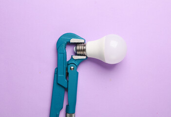 Metal adjustable wrench holding light bulb on purple background.