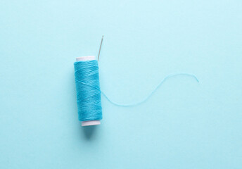 Skein of blue thread with needle, buttons on blue background. Sewing accessories