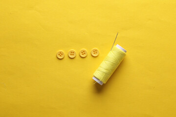 Skein of yellow thread and needle, buttons on yellow background. Sewing accessories