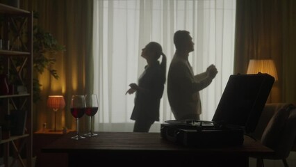 Vintage record player and glasses with red wine on the table close up. A young couple is dancing while enjoying a pleasant evening together. Silhouette. Slow motion. HDR BT2020 HLG Material.