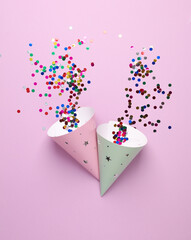 Birthday cone hats with confetti on pink background. Party concept. Top view