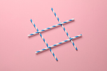 Cocktail tubes in the shape of a hashtag on a pink background. Minimalism party concept