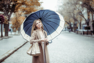 Happy woman in coat with umbrella holding shopping bags in city, autumn shopping sale