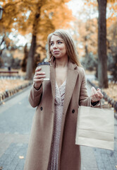 Happy woman in coat holding shopping bags and coffee cup outdoors, autumn shopping sale