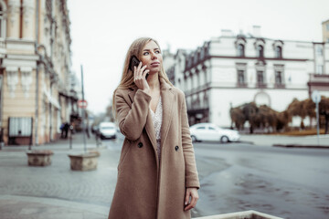 Fototapeta premium Young beautiful woman in a coat talking on the phone in European city