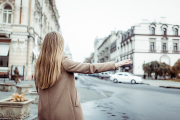 Fototapeta na wymiar Blonde woman catching car with hand gesture in european city