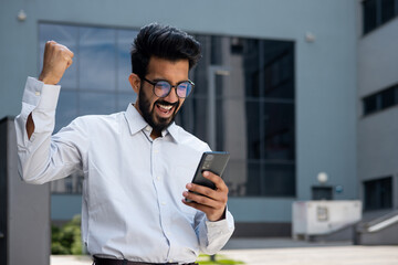 Indian man in a shirt walking outside an office building, a businessman received an online win...
