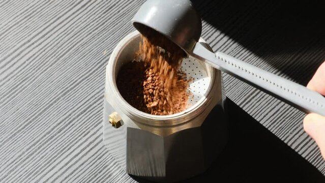 Putting ground coffee with measuring spoon in a moka pot on black background