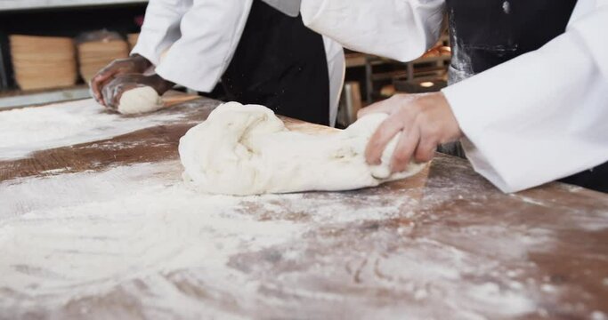 Diverse bakers working in bakery kitchen, kneading dough on counter in slow motion