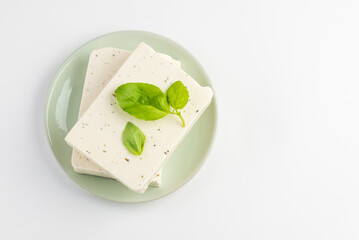 Top view of  tofu, paneer or soy cheese with fresh basil leaves in a green plate isolated with copy...