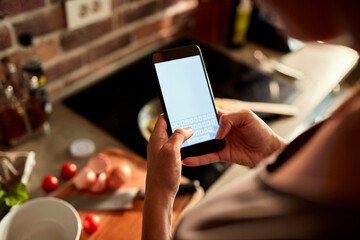 Young woman using a smart phone while cooking in the kitchen