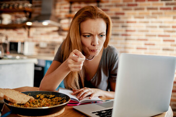 Young woman using a laptop while having breakfast in the morning