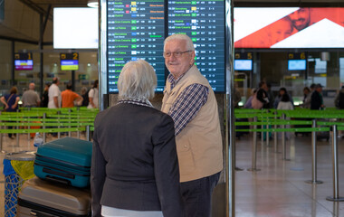 Back view of white haired senior couple pushing luggage trolley walking in the airport area for departure. Old senior man and woman leaving for vacation