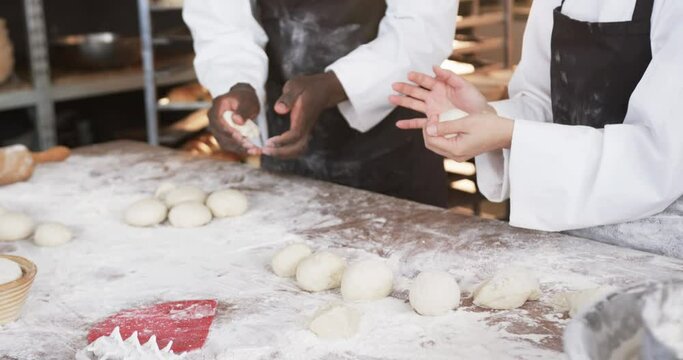 Happy diverse bakers working in bakery kitchen, making rolls from dough in slow motion