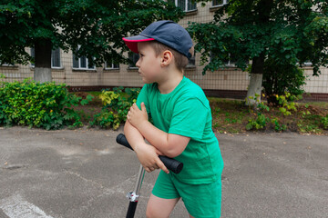 The boy is leaning on the steering wheel of the scooter