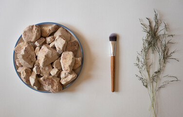 White clay stones with dried leaves and a makeup brush on a white background