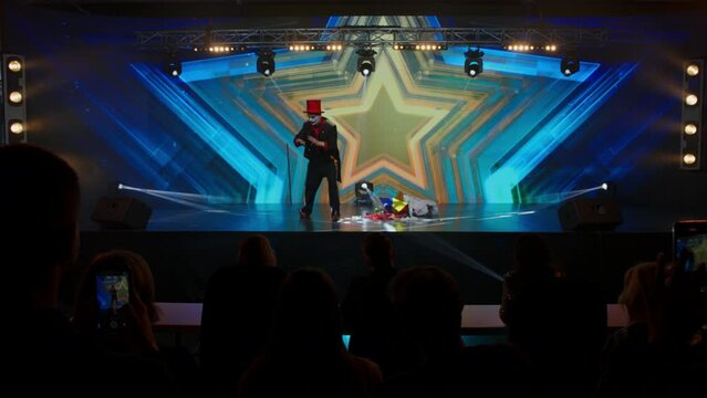 Creepy clown mime showing magic tricks with a flying stick on stage during talent show audition. Broadcast television style TV entertainment program 