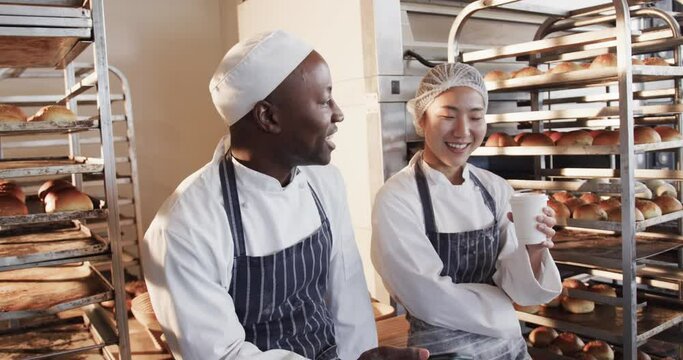 Happy diverse bakers working in bakery kitchen, using smartphone in slow motion