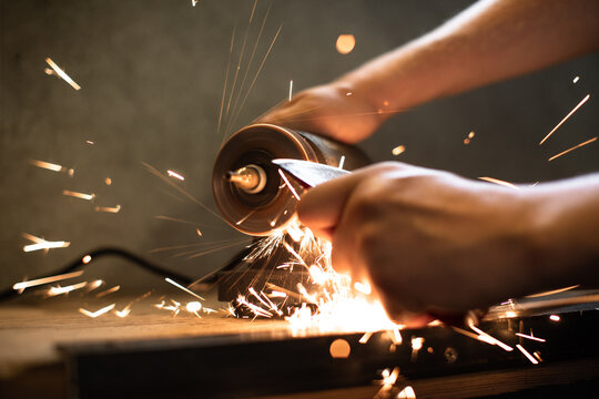 Close-up of men's hands sharpening an axe on an electric sharpener. Repair of home tools. 
Sparks fly.