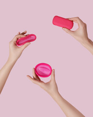Female hands with reusable menstrual disc on pink background