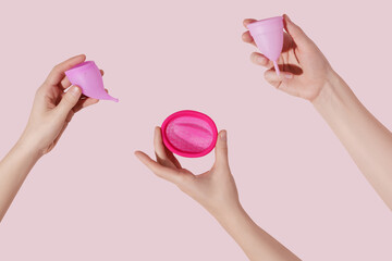 Female hands hold reusable menstrual disc and cups on pink background