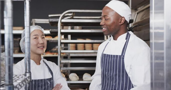 Portrait of happy diverse bakers in bakery kitchen with arms crossed in slow motion