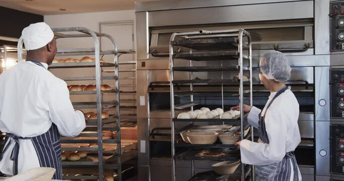 Happy diverse bakers in bakery kitchen preparing rolls in slow motion