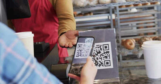 Diverse worker and customer scanning qr code with smartphone in bakery in slow motion