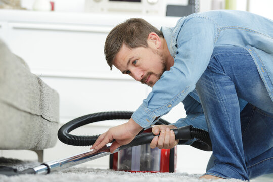 Man Cleaning A Floor Under A Bed With Vacuum Cleaner